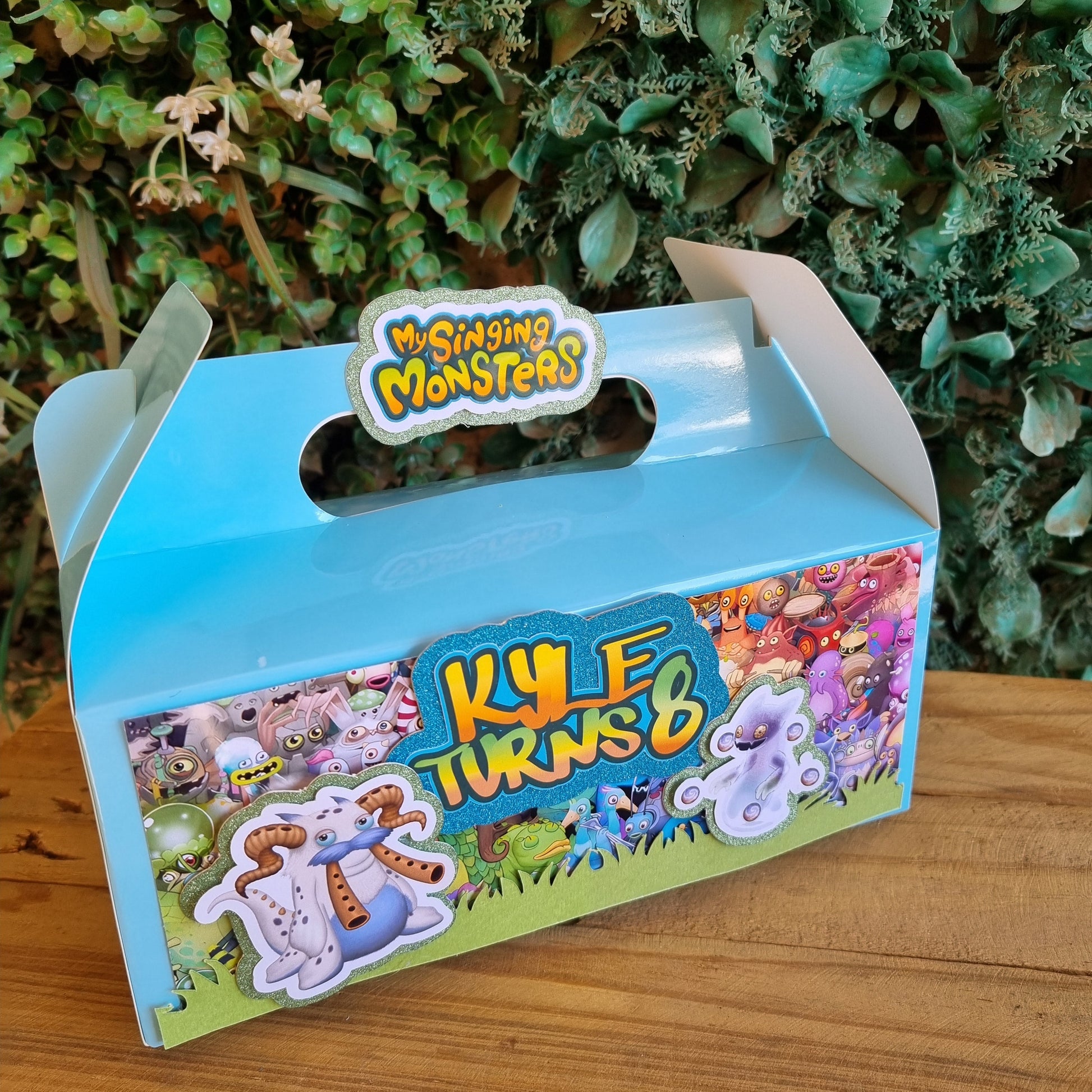 Children's toy box with colorful design on a wooden surface and green plants in the background
