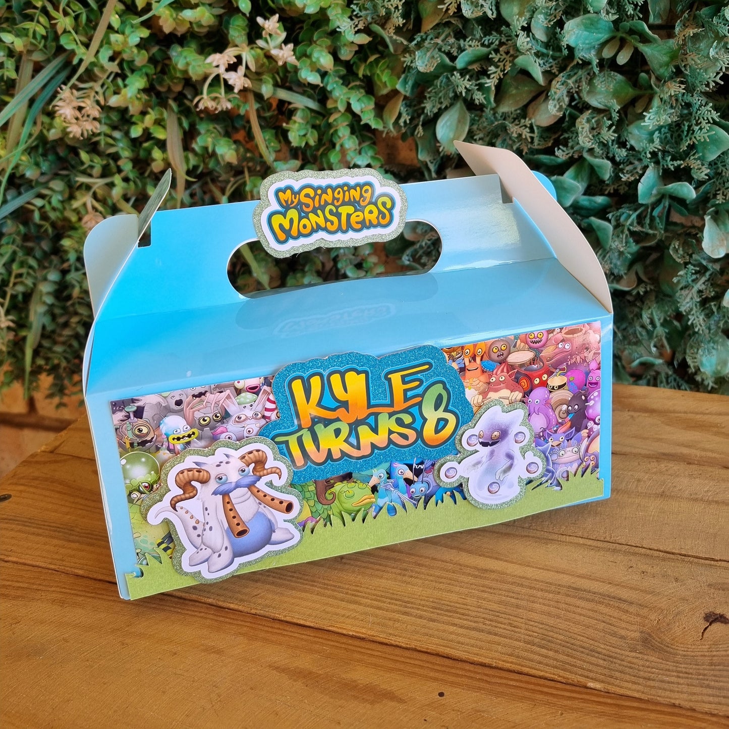 Children's puzzle box with colorful design on a wooden surface and green plants in the background