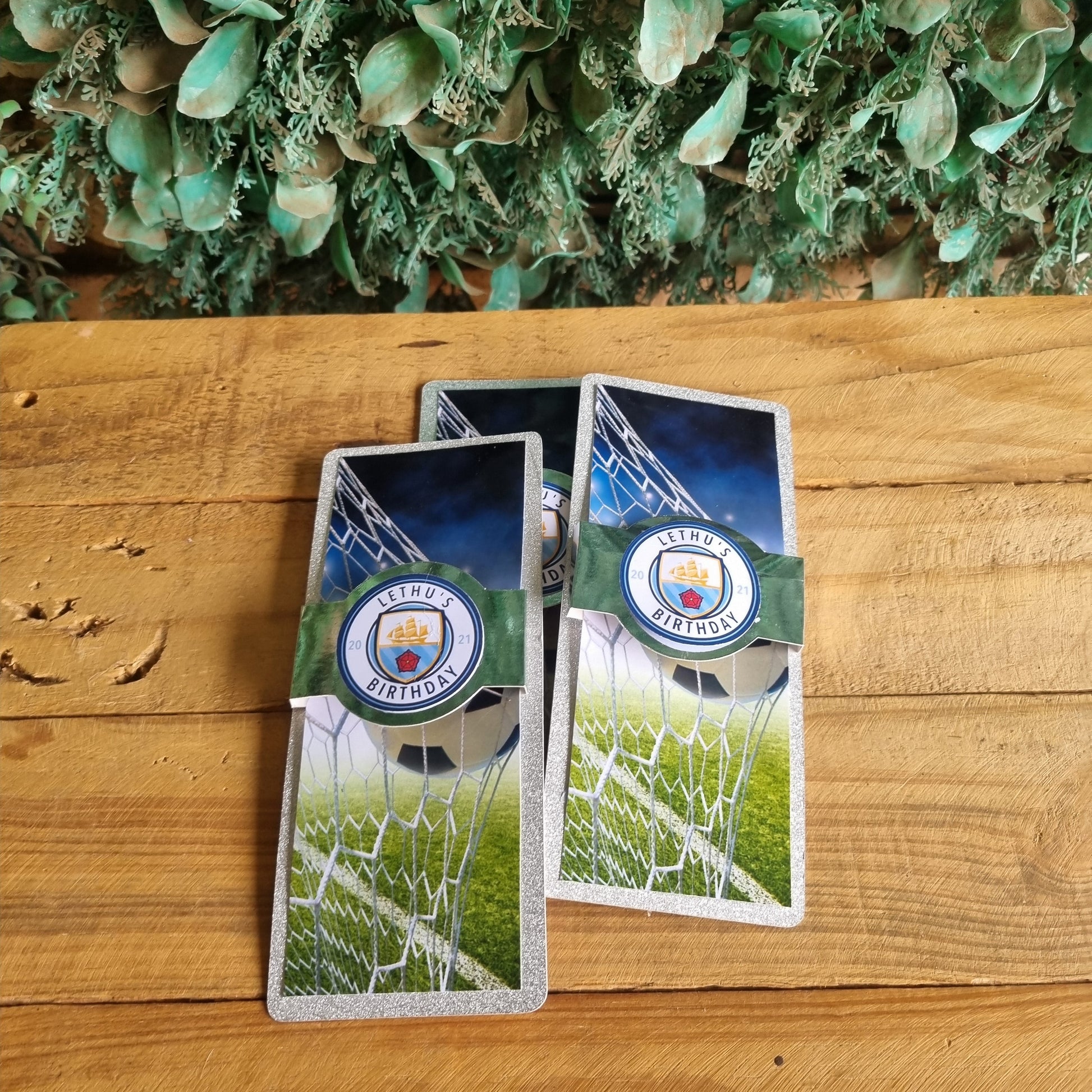 Two playing cards with sports-themed designs on a wooden surface next to green foliage.