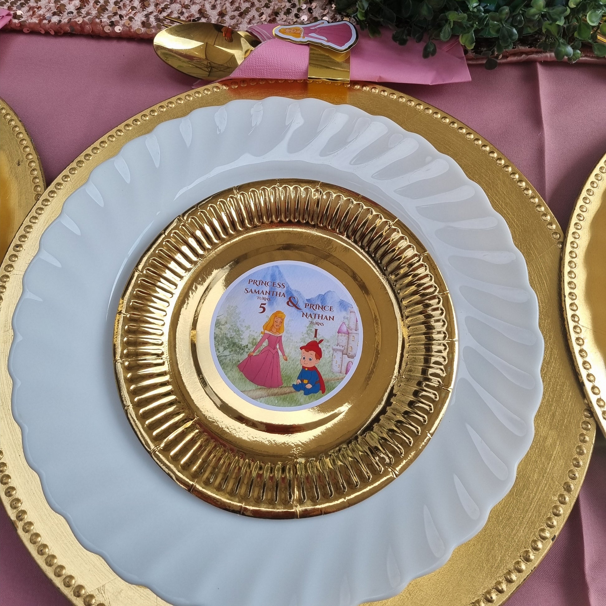 Decorative table setting with gold-rimmed plates and a pink napkin.