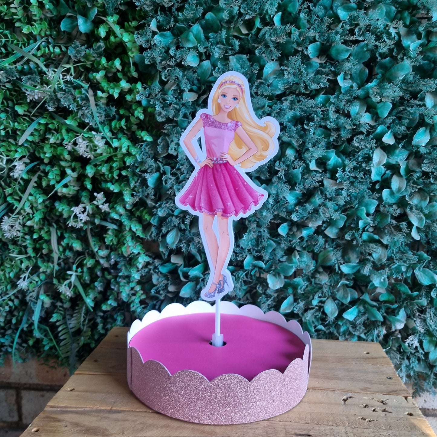 Pink fairy cake with a fairy figure on a wooden surface and green foliage background