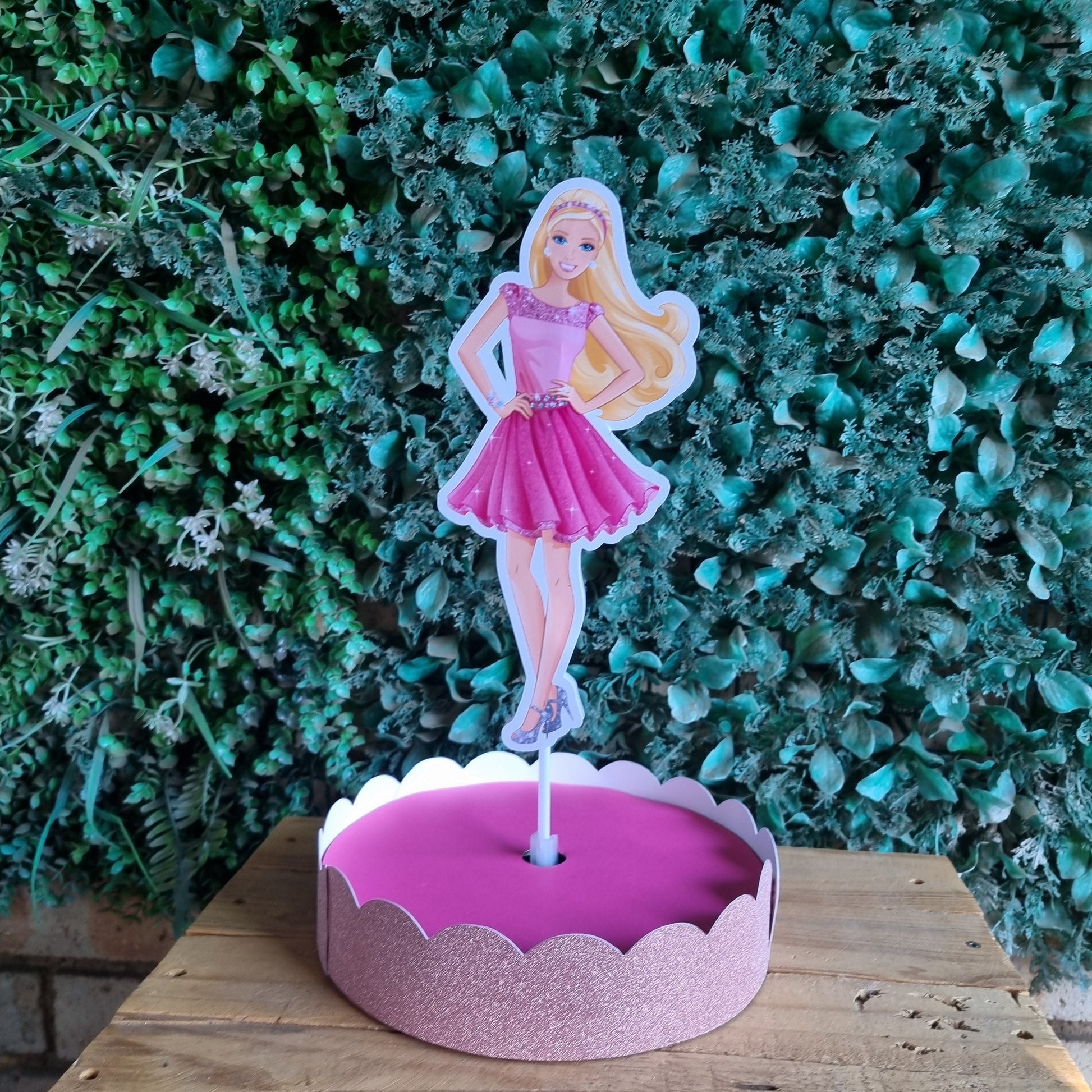 Pink fairy cake with a fairy figure on a wooden surface and green foliage background