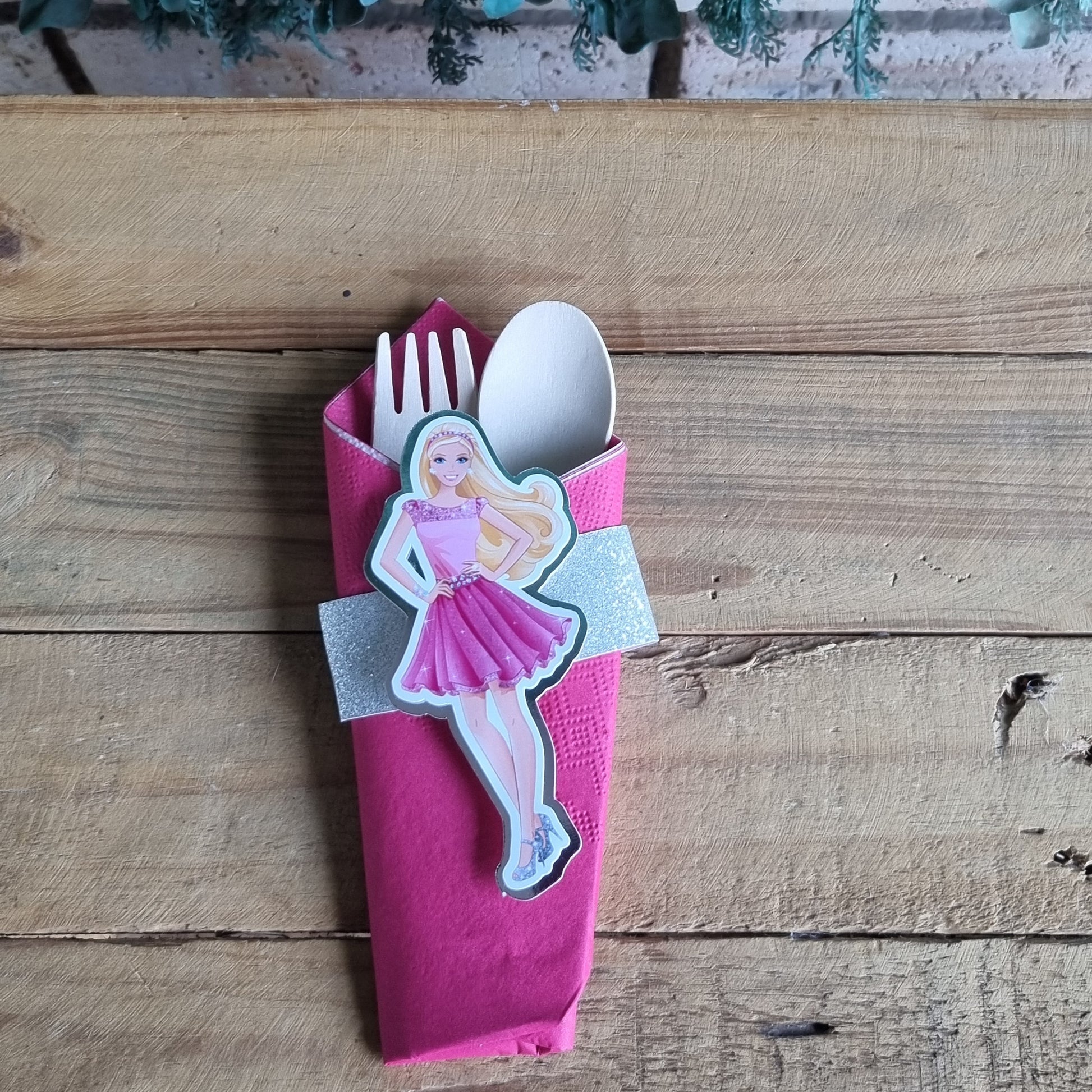 Pink toy with a spoon and fork on a wooden surface next to greenery