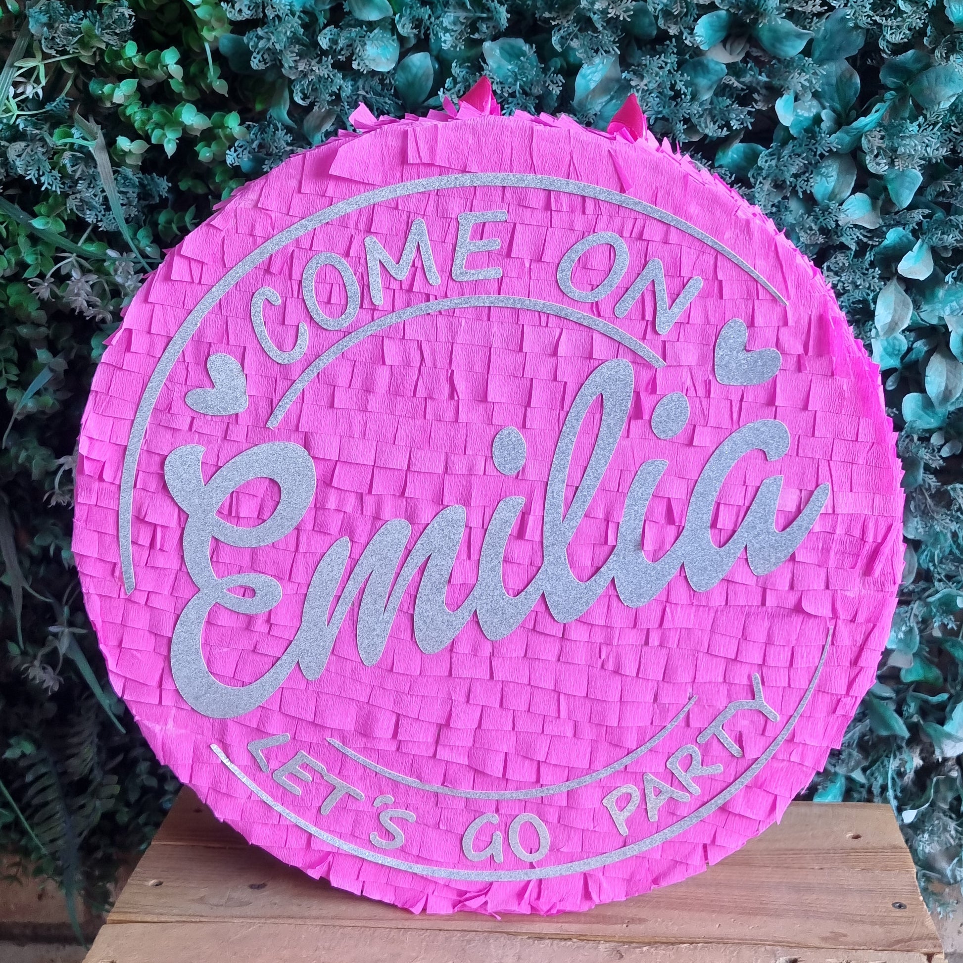 Pink piñata with silver text against a green leafy background