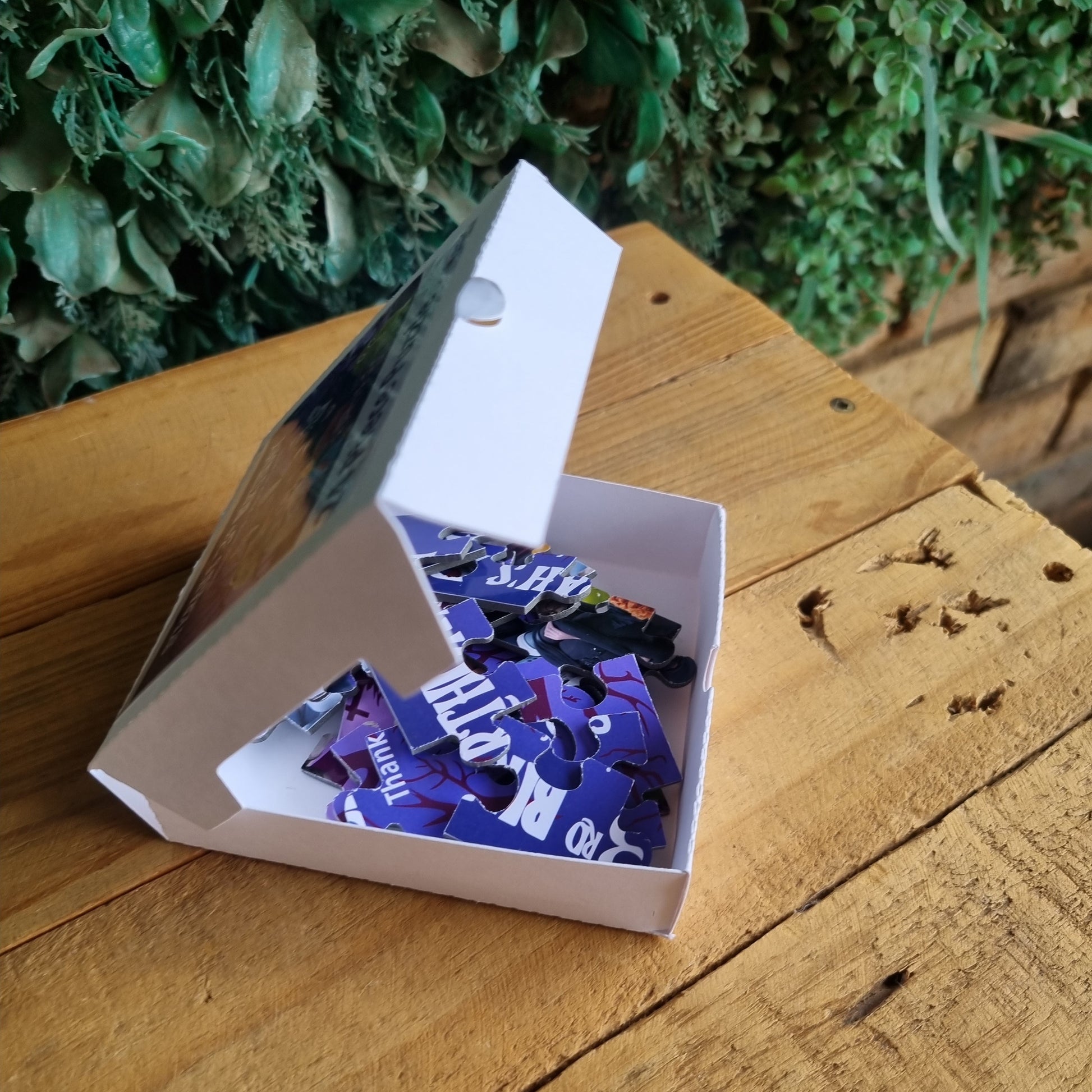 Open box with purple items on a wooden surface next to greenery