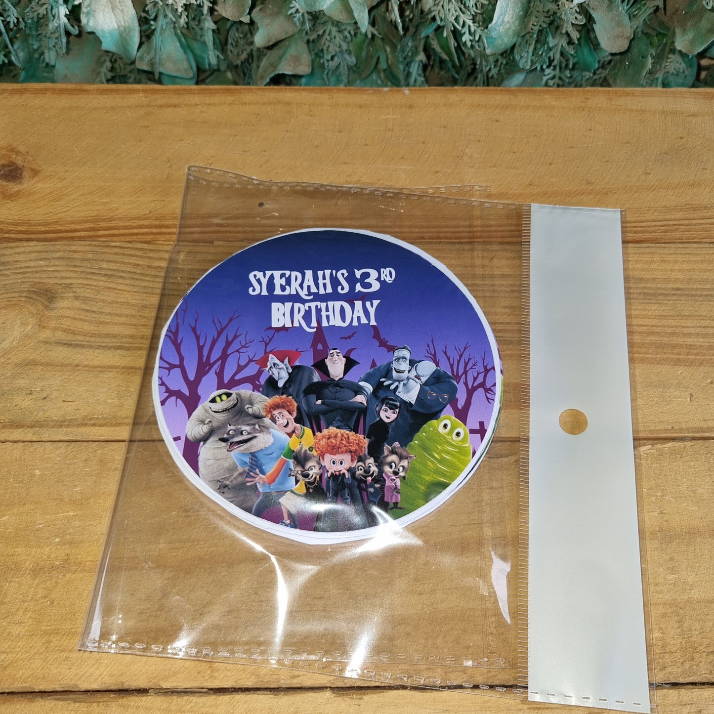 Round purple sticker with cartoon characters on a clear plastic sheet over a wooden surface.