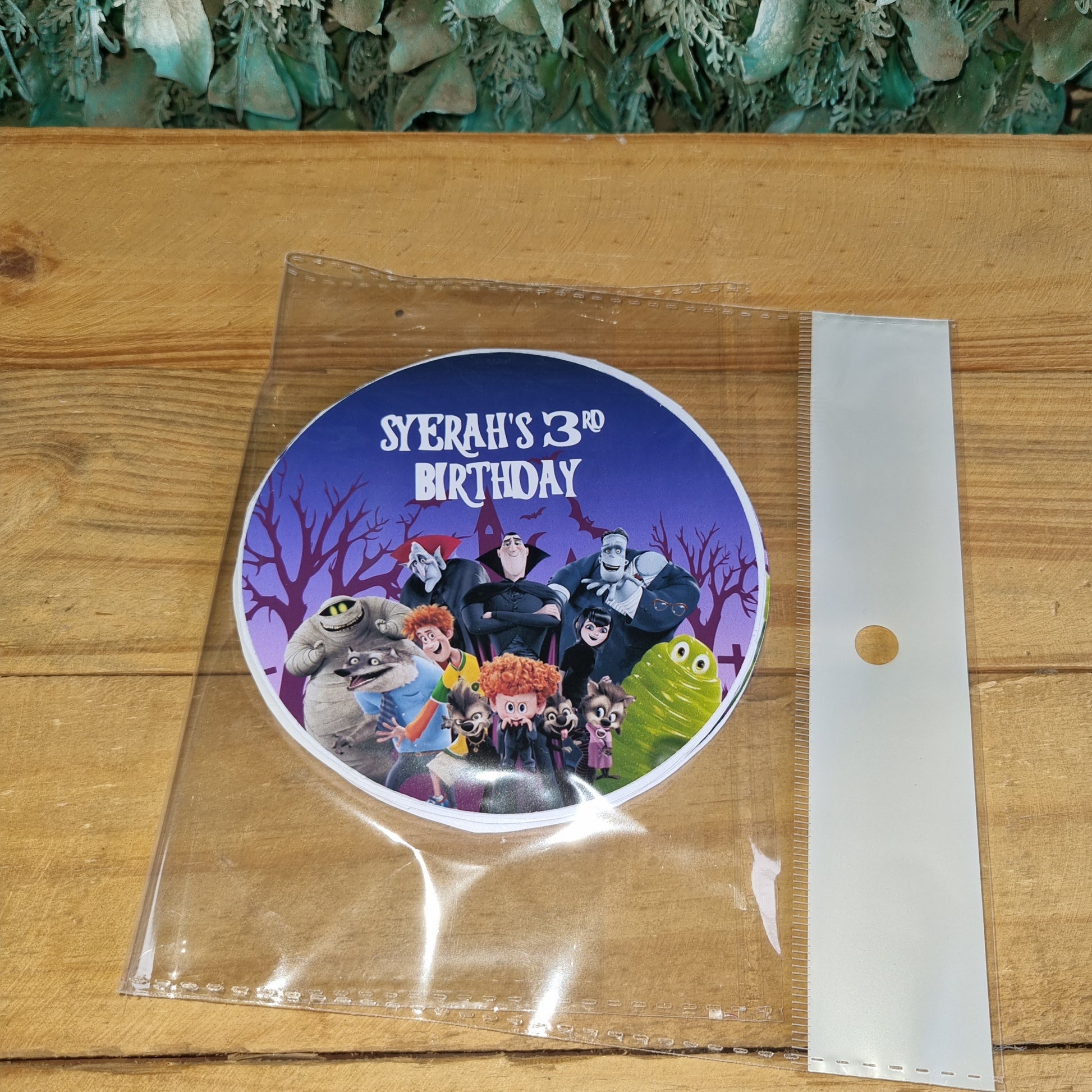Round purple sticker with cartoon characters on a clear plastic sheet over a wooden surface.