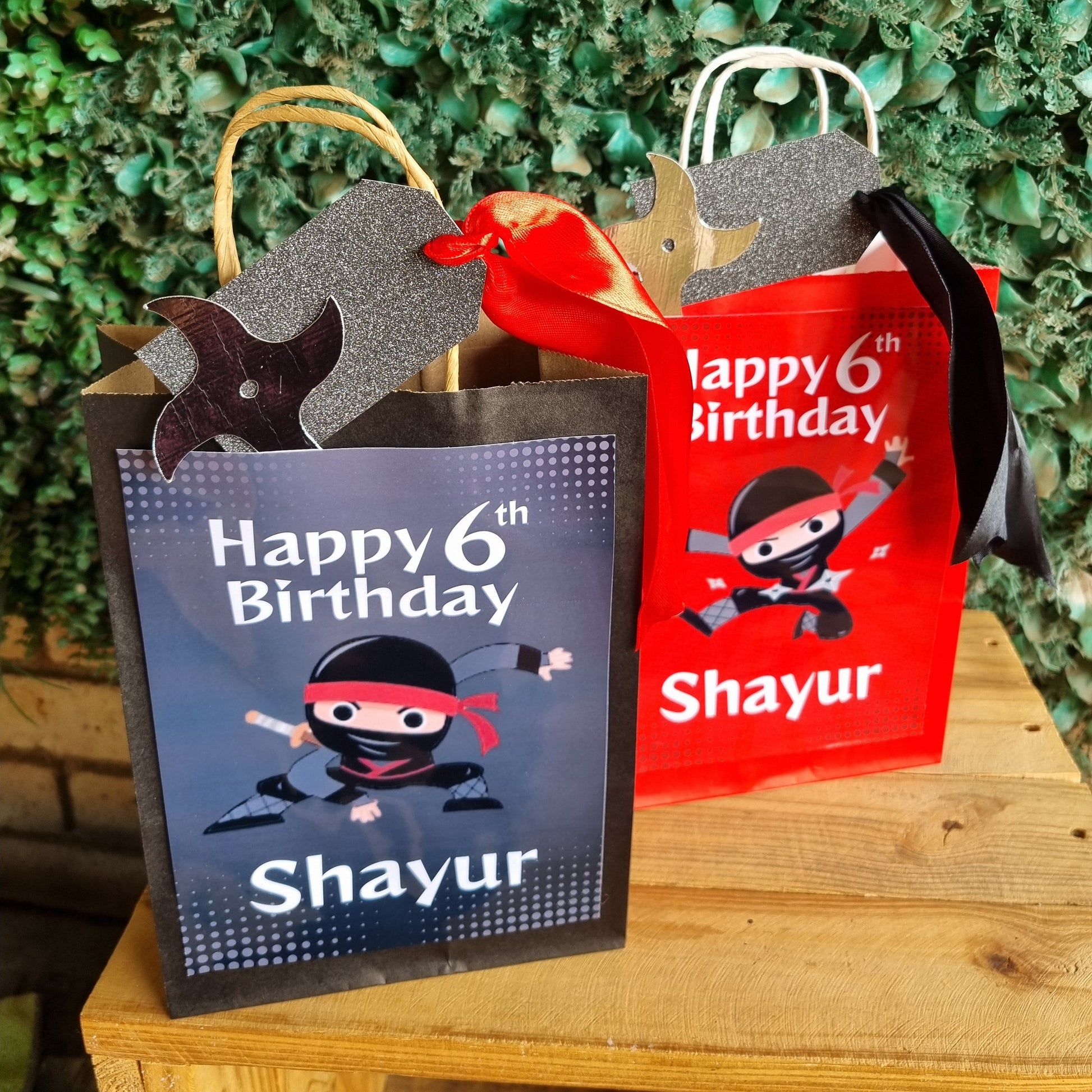 Two birthday gift bags with a pirate theme and 'Happy 6th Birthday Shayur' text against a green leafy background.