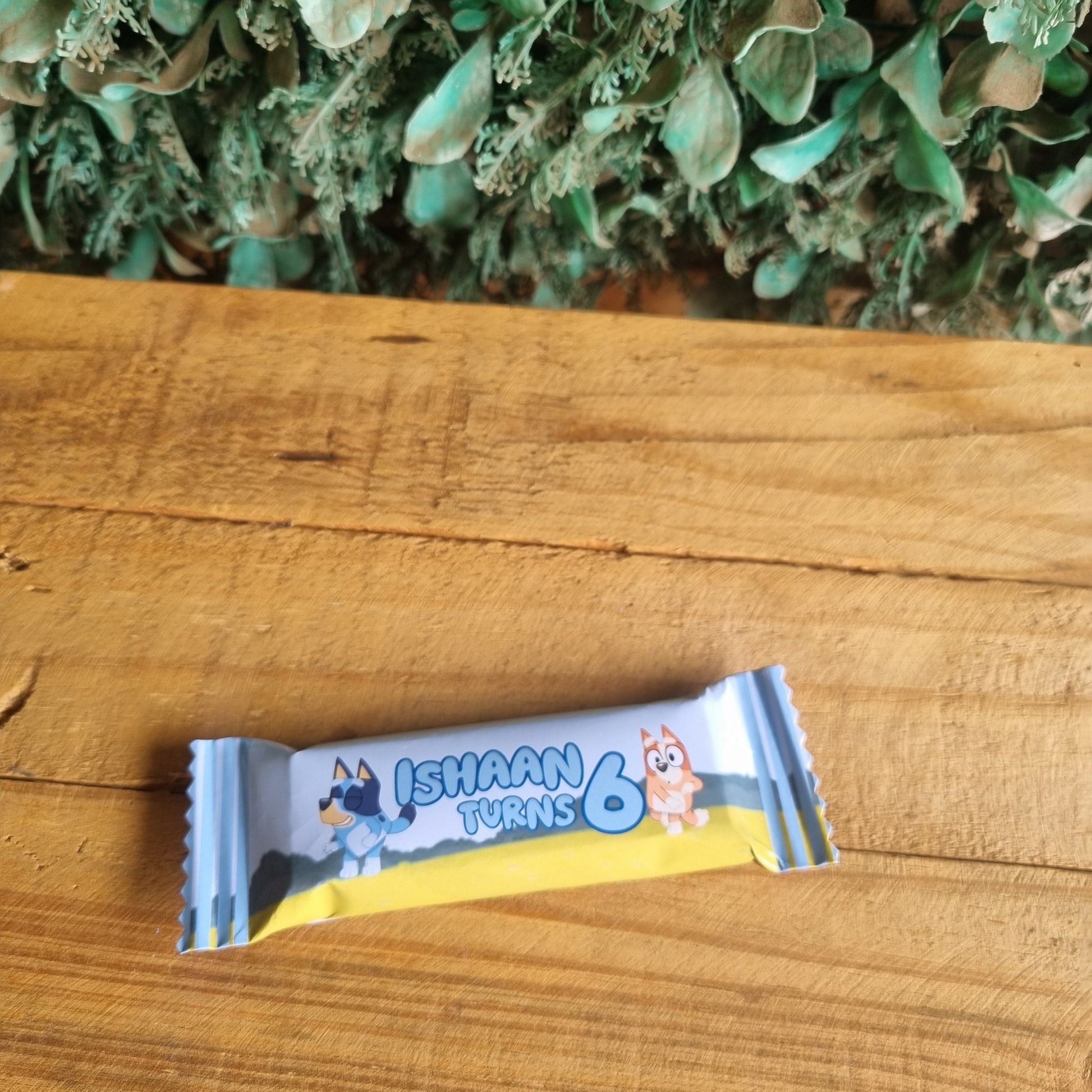 Cartoon character on a chocolate bar wrapper on a wooden surface with greenery.