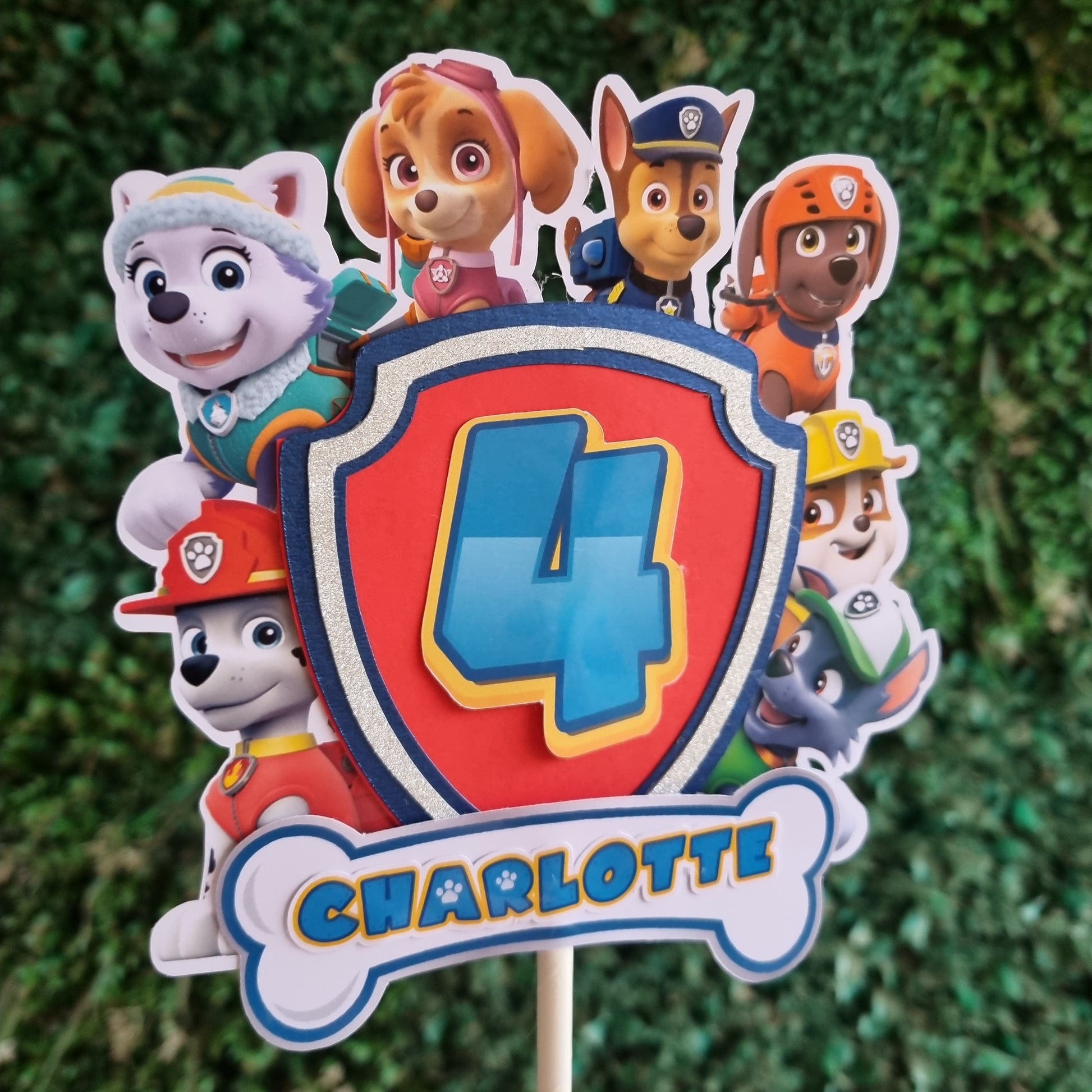 Paw Patrol-themed cake topper with character faces on a grass background