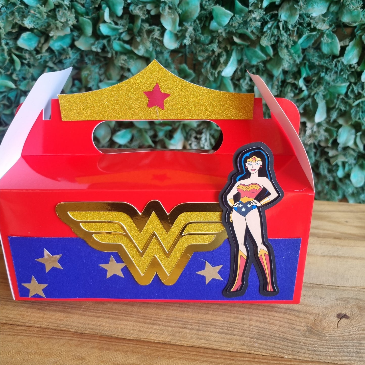 Decorative letter 'J' with Wonder Woman design on a wooden surface and green foliage background