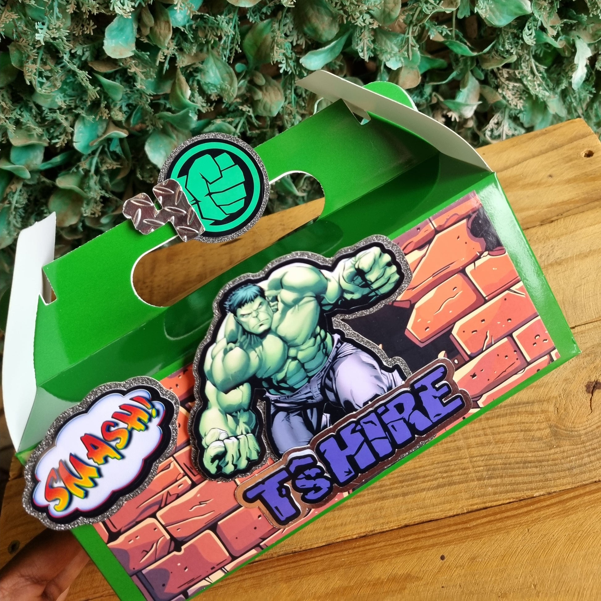 Green box with superhero design on a wooden surface and greenery background