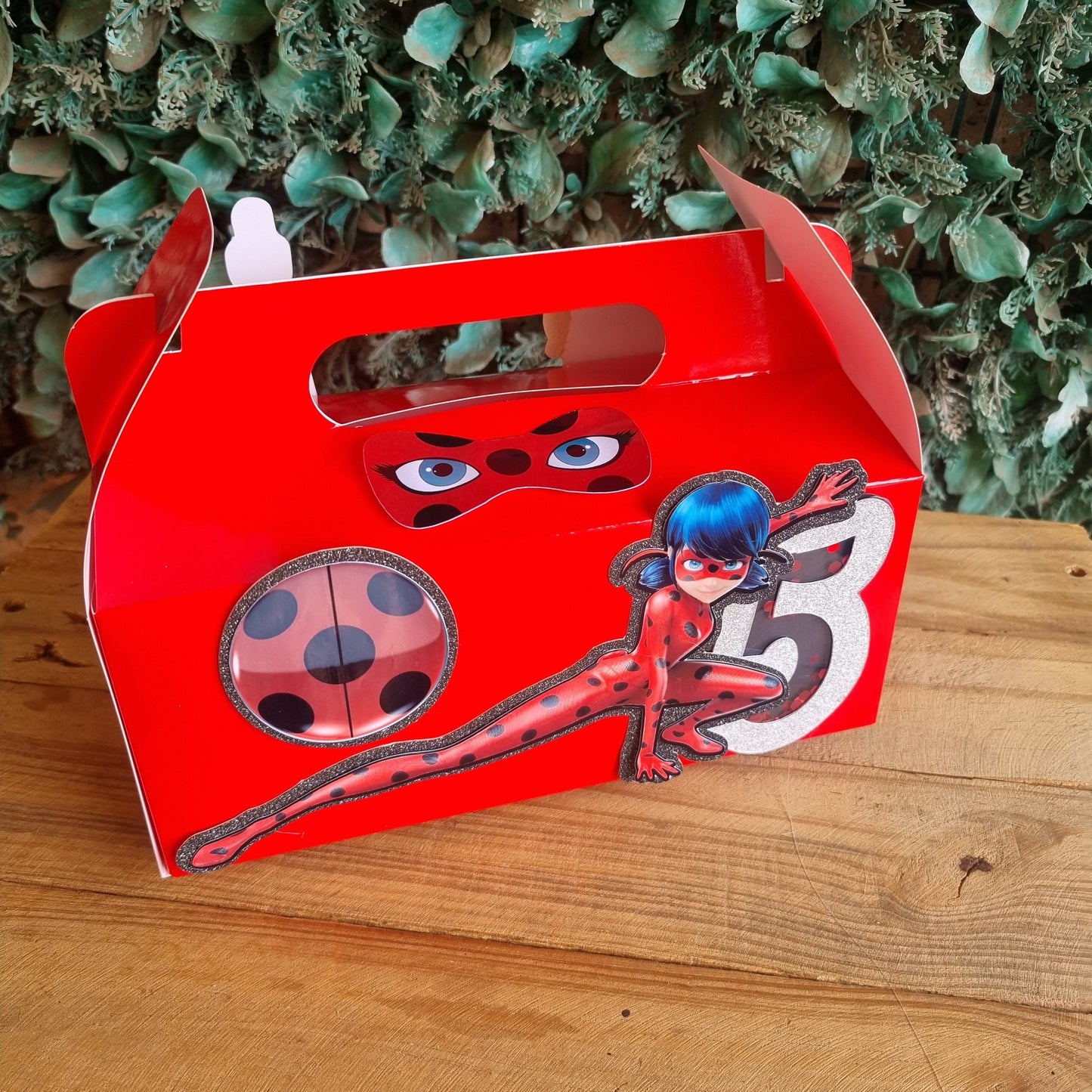 Red ladybug-shaped object on a wooden surface with greenery in the background