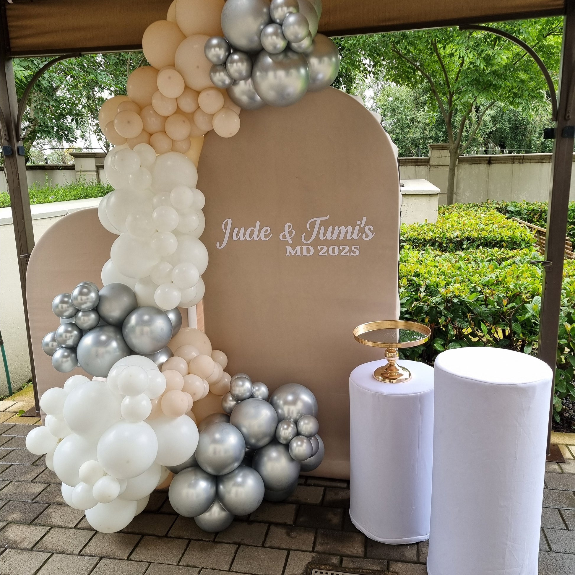 Decorative arch with balloons and 'Jade & Tom's' text, outdoor setting