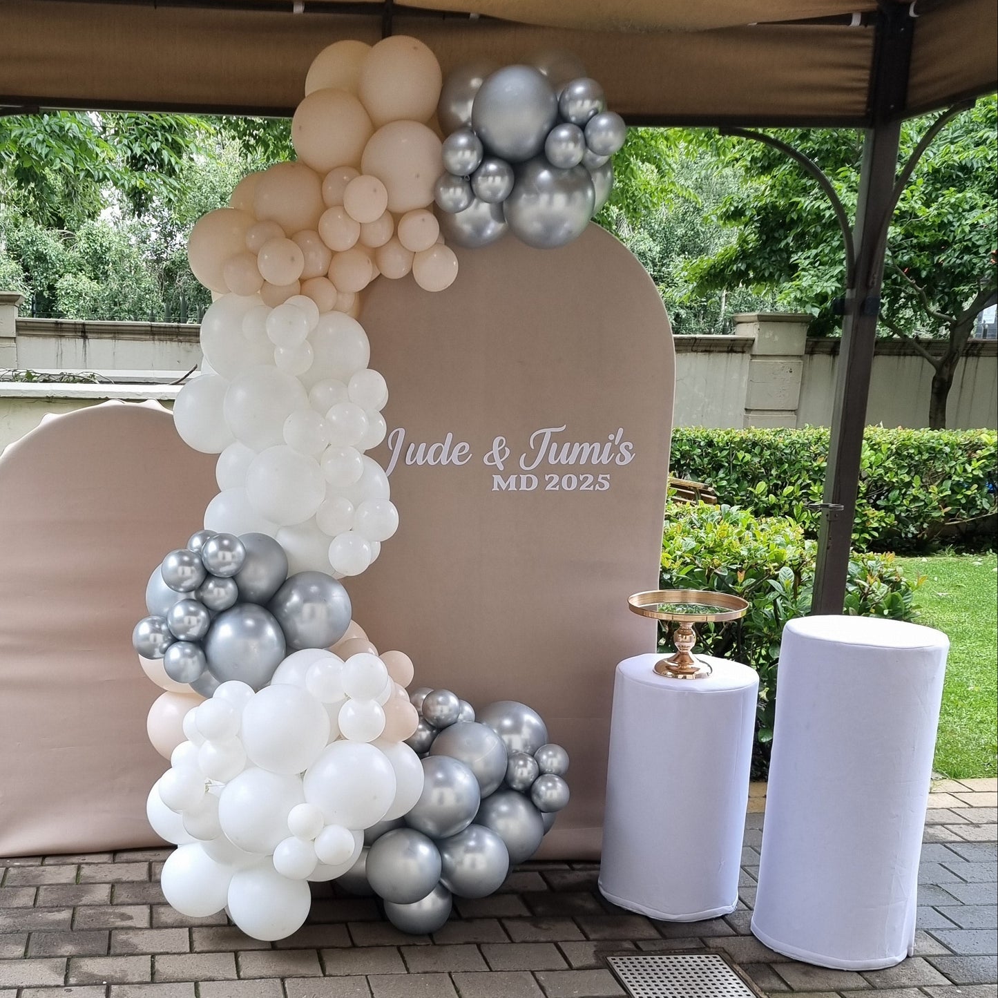 Decorative arch with balloons and a banner on a paved walkway