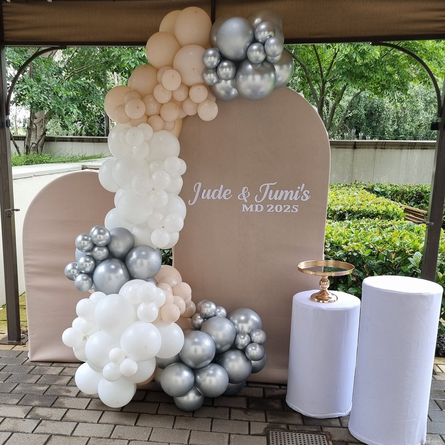 Decorative arch with balloons and a sign on a paved walkway