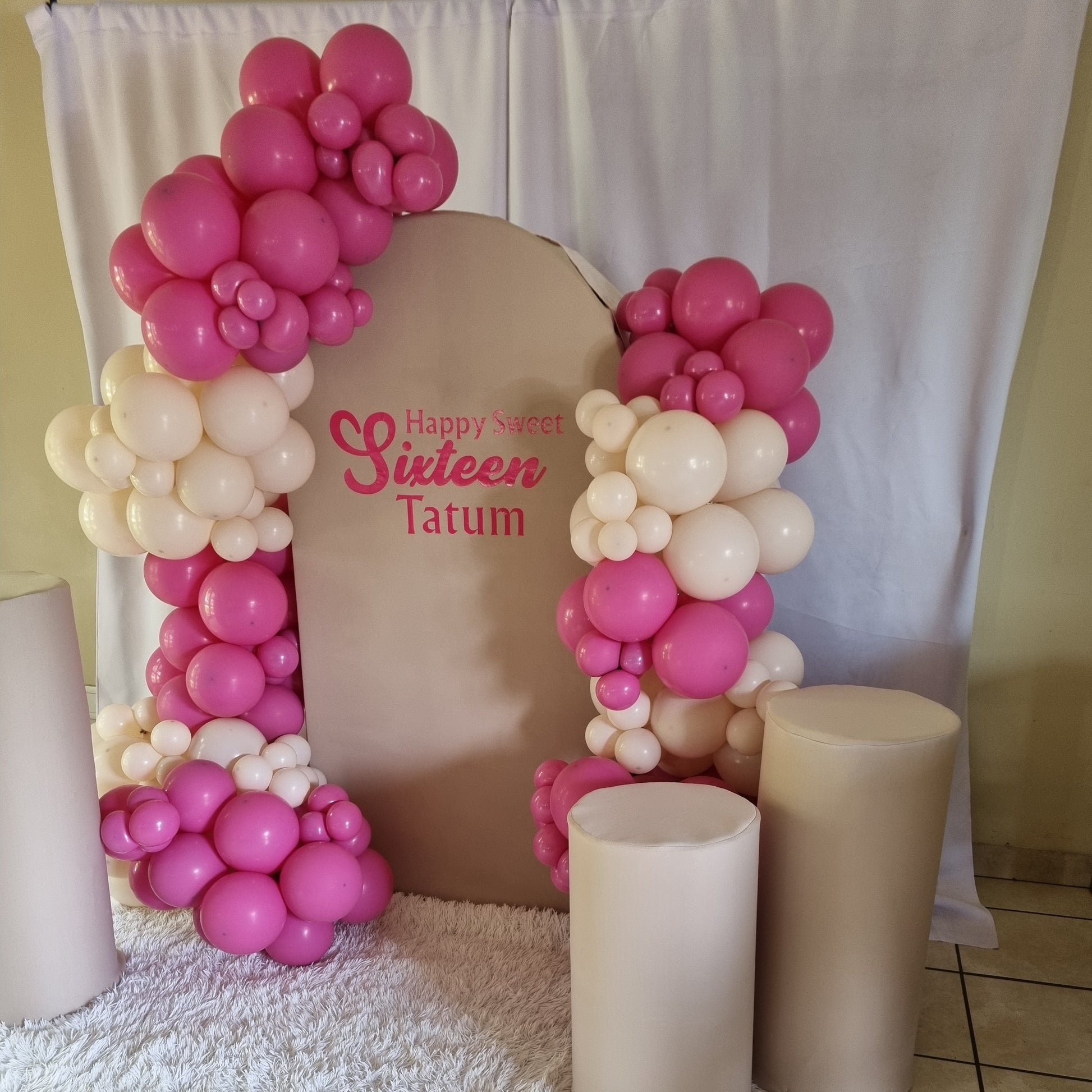 Decorative arch made of pink and white balloons with 'Happy Sweet 16' text on a cushion.