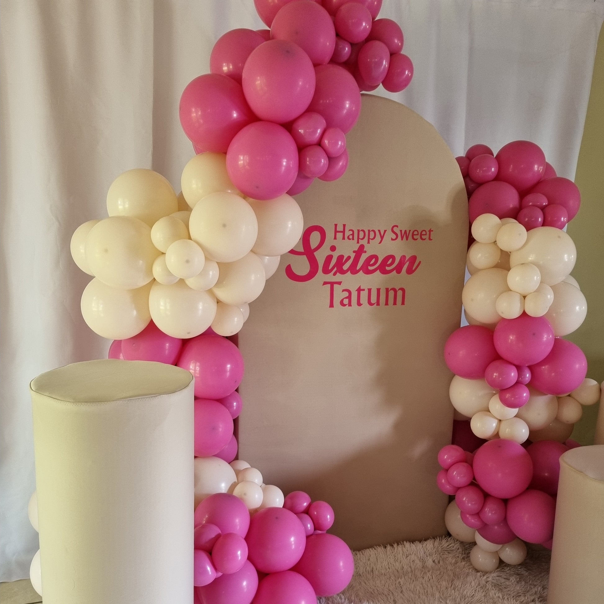 Decorative arch made of pink and white balloons with 'Happy Sweet Sixteen' text on a cushion.