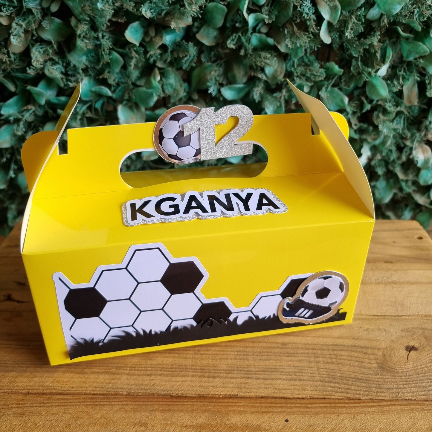 Yellow birdhouse with soccer ball design and 'KGANIA' branding against a wooden background.