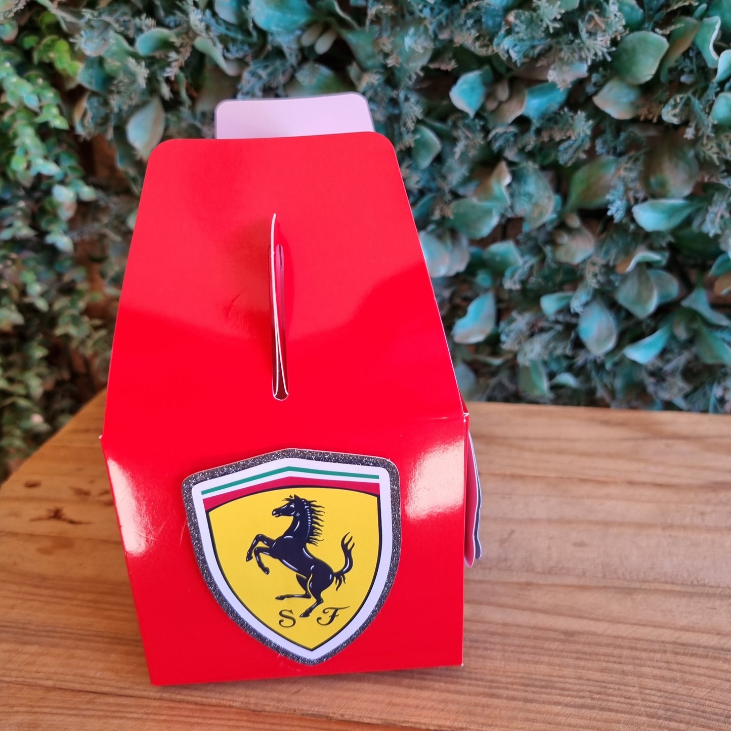 Red Ferrari car model on a wooden surface with greenery in the background