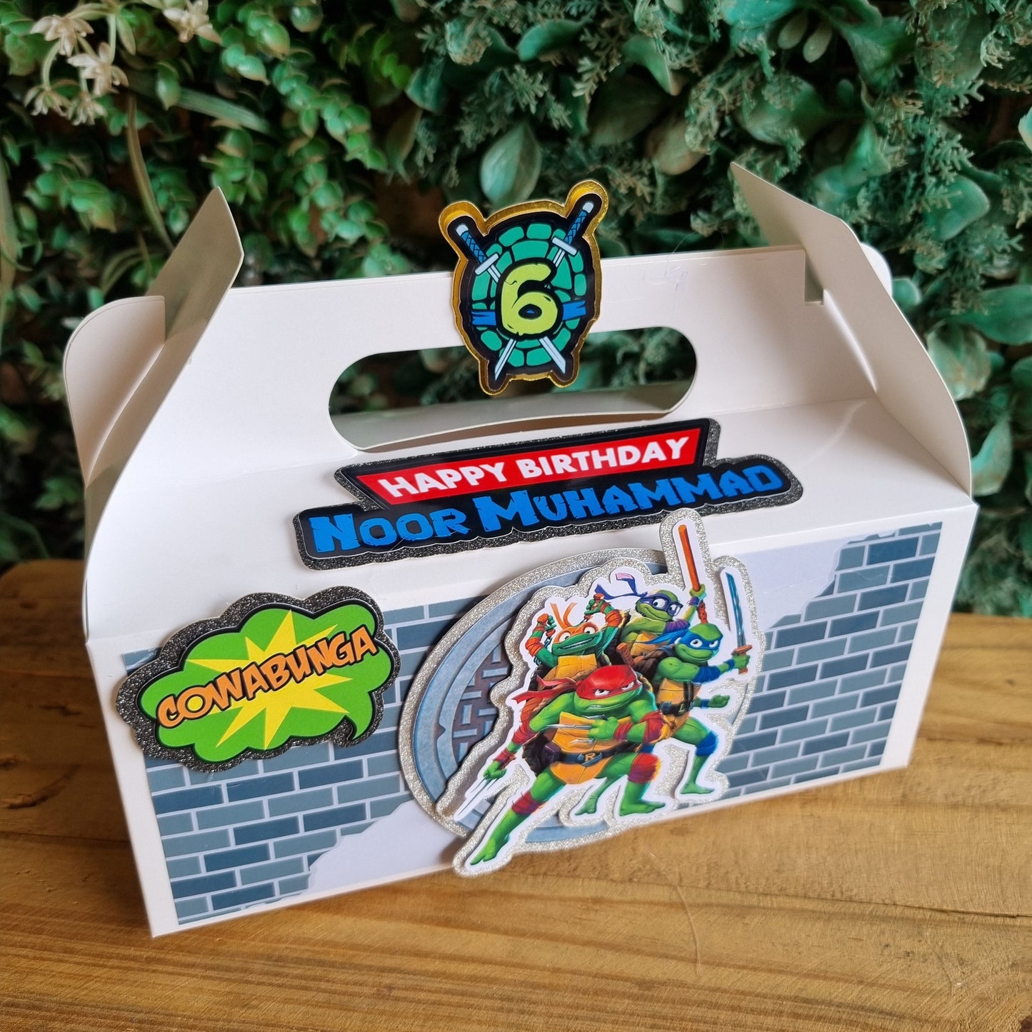 Carton with birthday stickers on a wooden surface and green foliage background