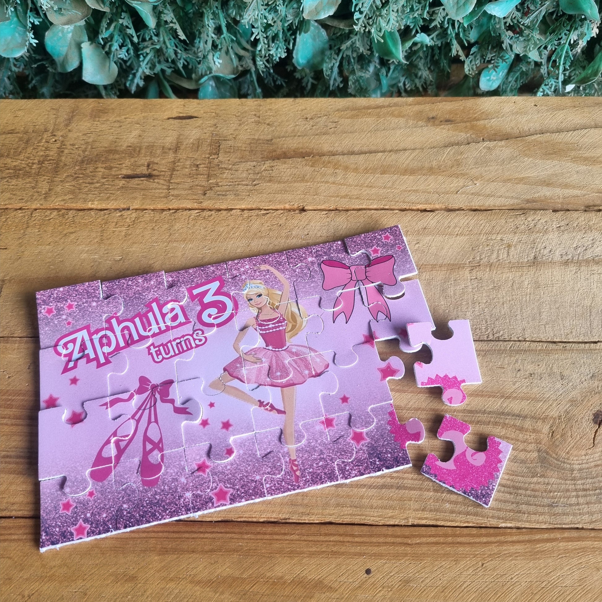 Barbie-themed puzzle on a wooden surface with greenery on the side