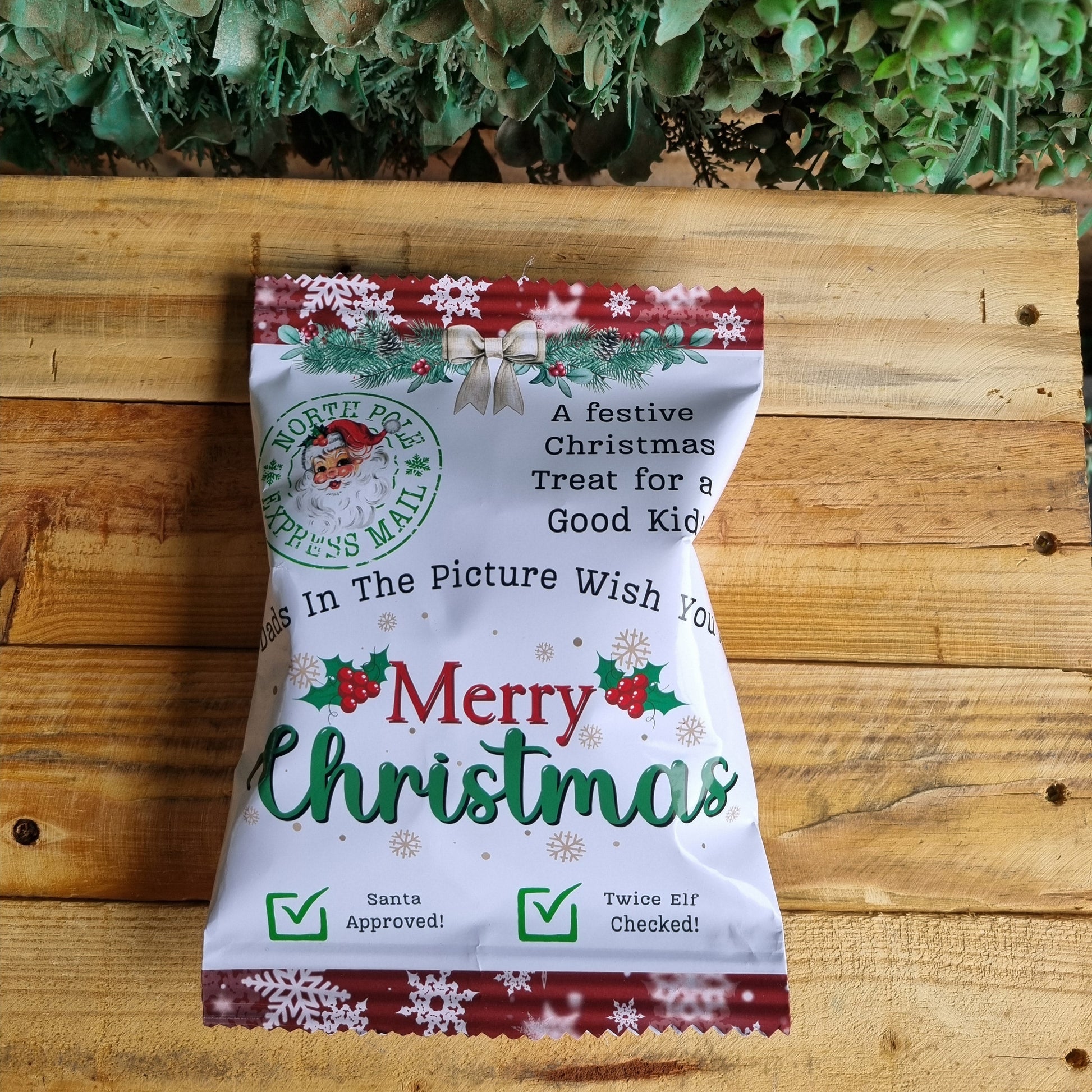 Christmas-themed product packaging on a wooden surface with greenery in the background