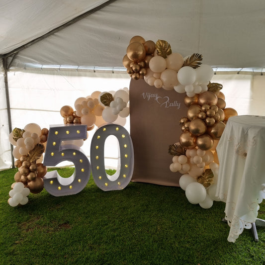 Decorative arch with balloons and a '50' sign on a grassy area.