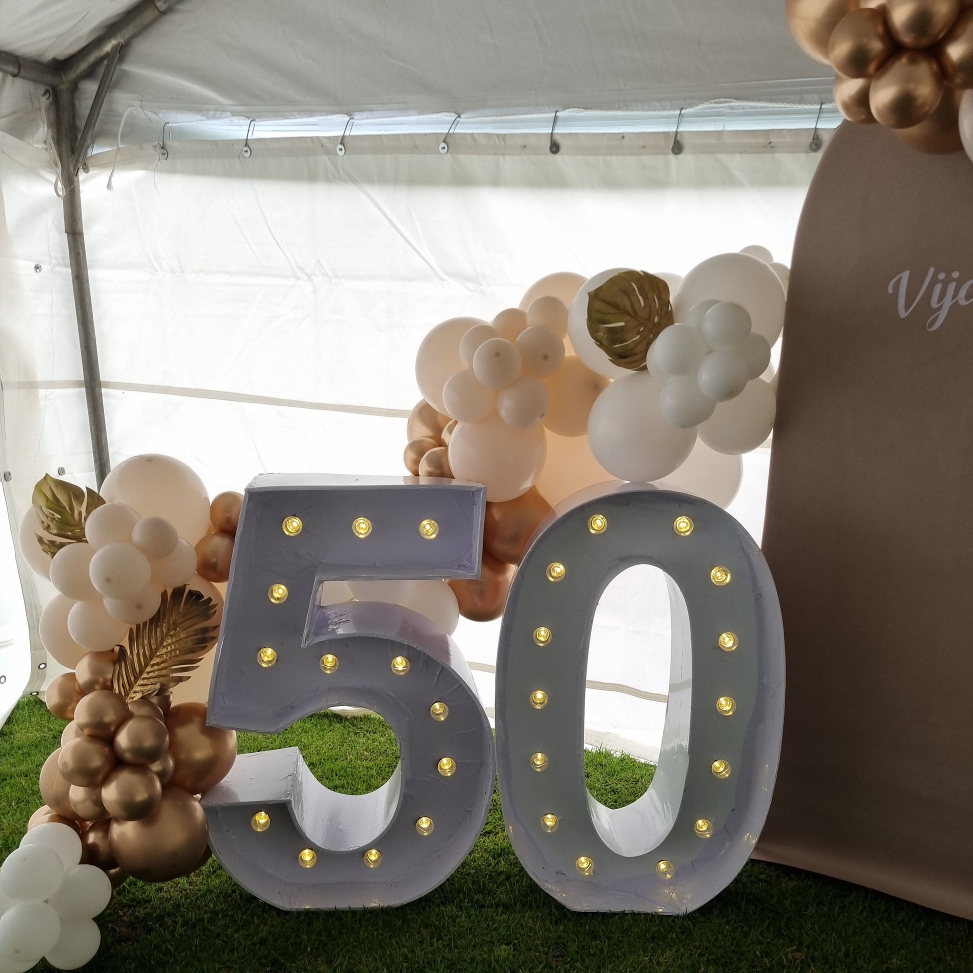 Decorative LED letters spelling 50' with balloons and flowers on a grassy background