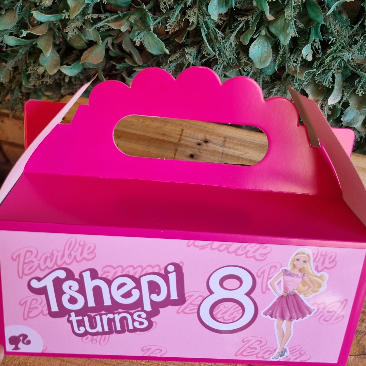 Pink birthday cake box with a wooden handle on a green leafy background