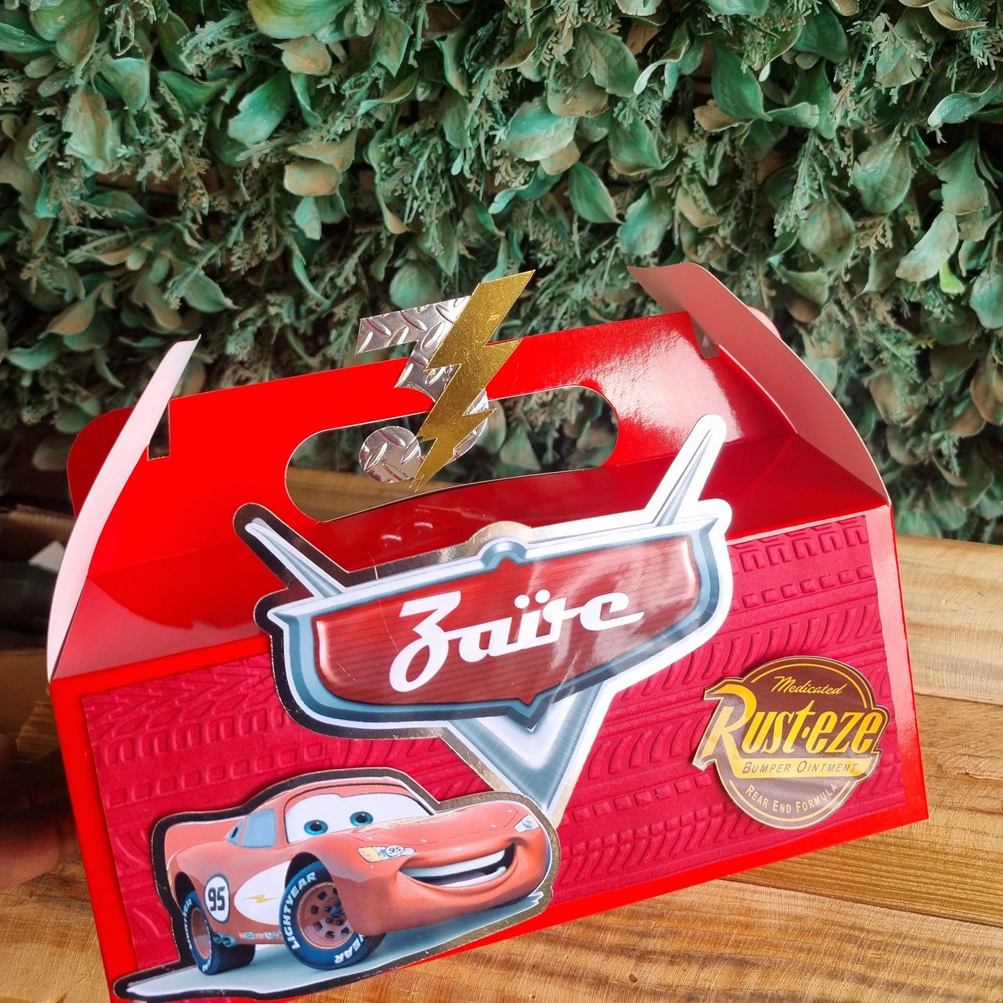 Red box with a character design on a wooden surface next to green leaves