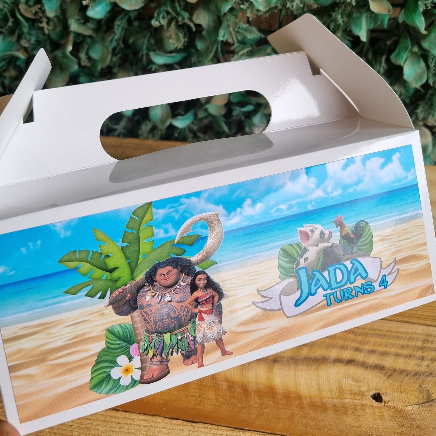 Product packaging with a tropical design featuring characters and text, placed against a green leafy background.