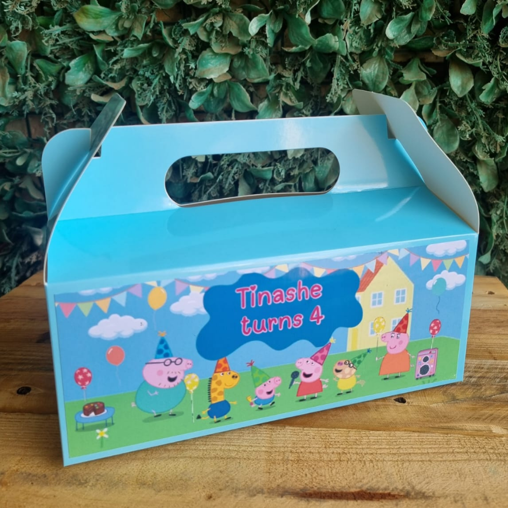 Children's birthday party favor box with cartoon characters and text 'Tinashe turns 4' against a green leafy background.