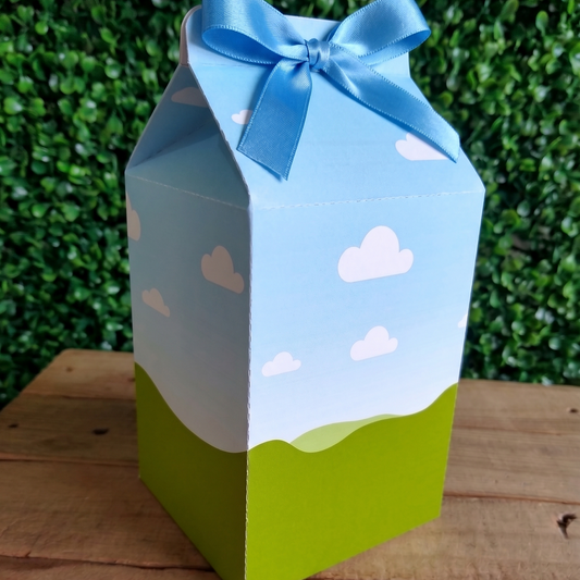 Carton box designed like a milk carton with a blue sky and clouds pattern, on a wooden surface with a green leafy background.
