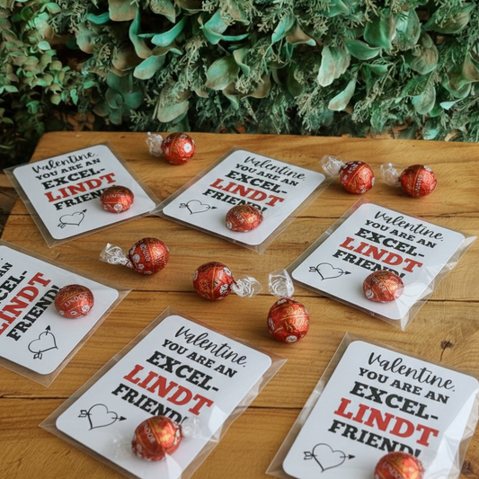 Valentine's Day cards with Lindt chocolate pieces on a wooden surface with greenery in the background