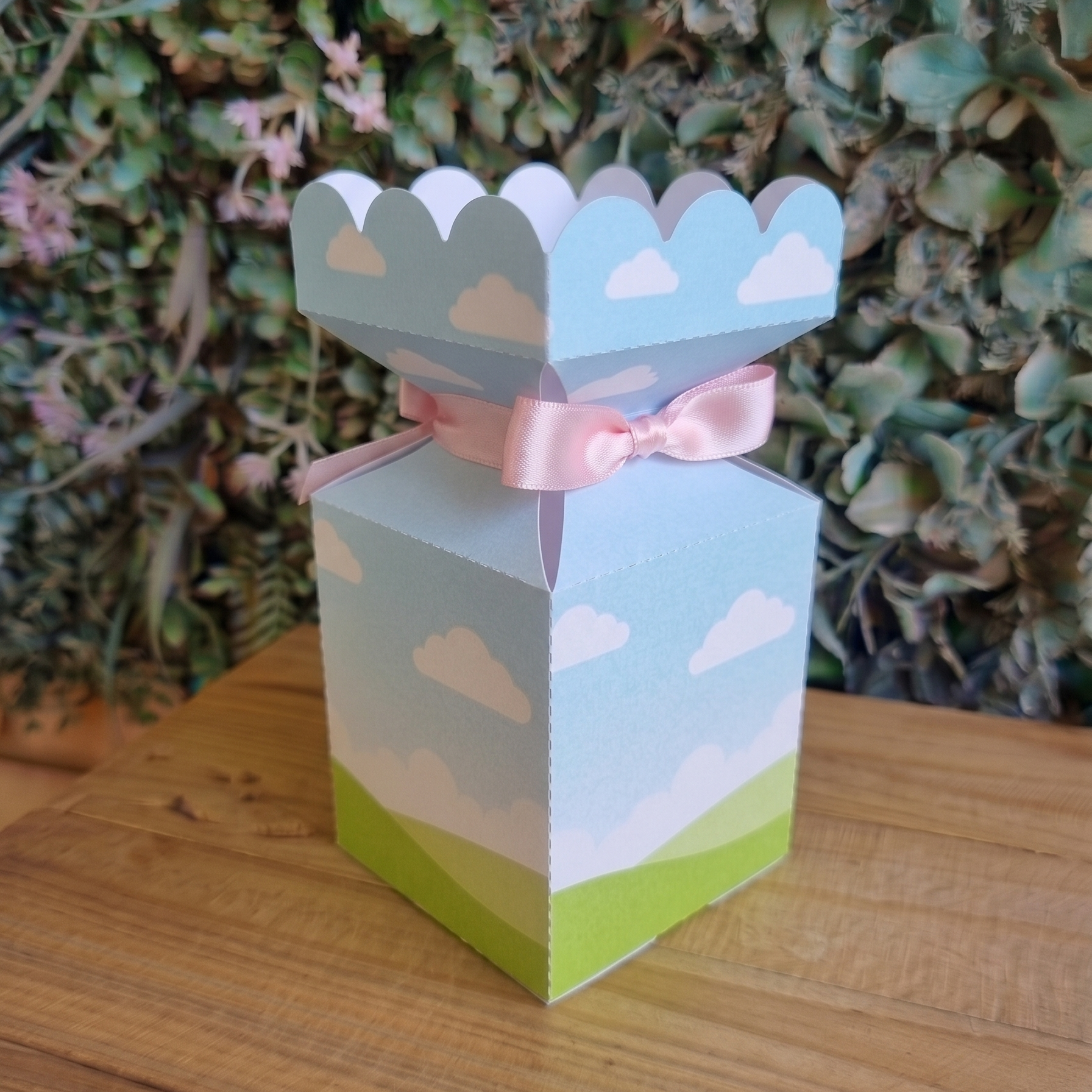 Decorative gift box with a pink ribbon on a wooden surface with a green plant background