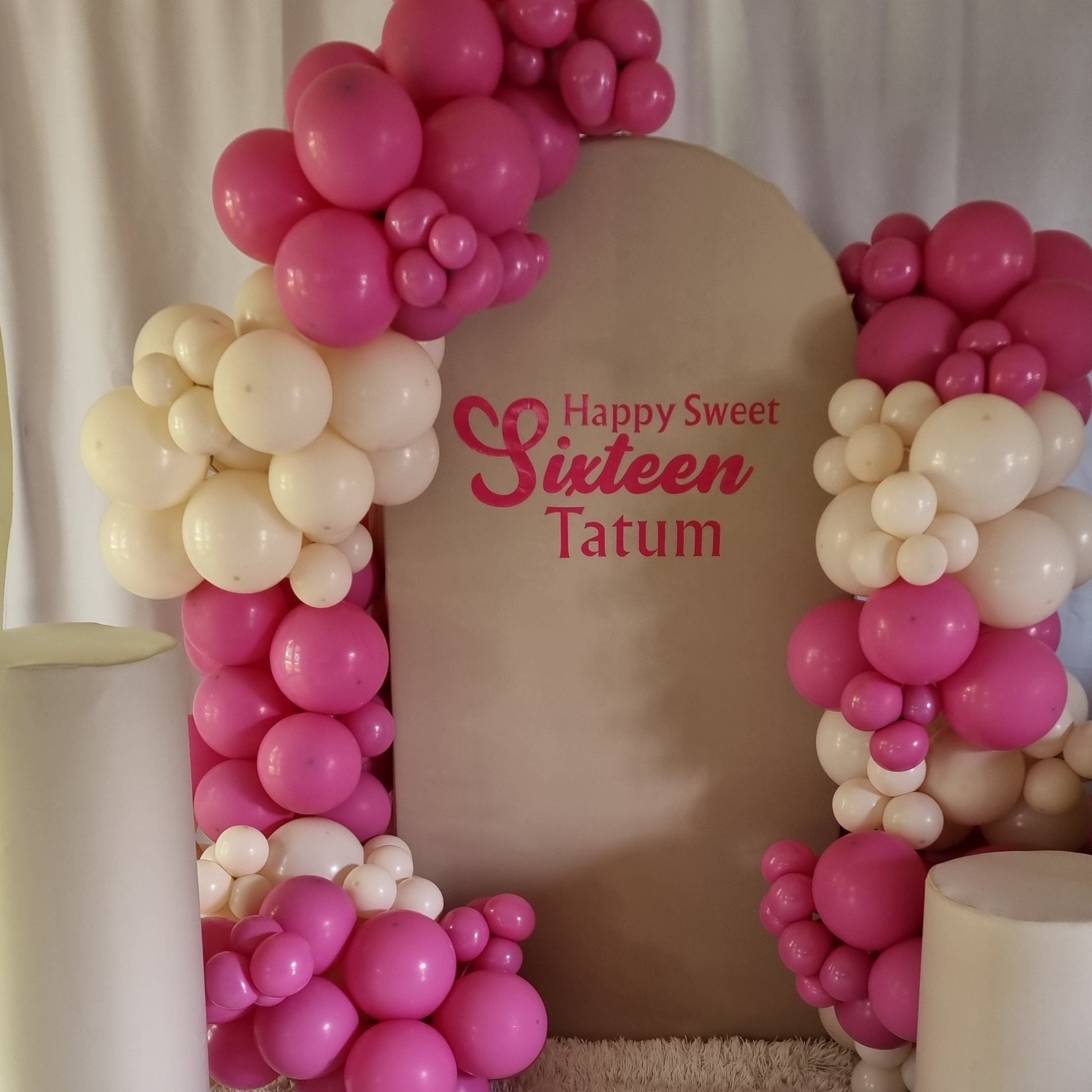 Decorative balloon arch with 'Happy Sweet Sixteen Tatum' text on a textured surface.