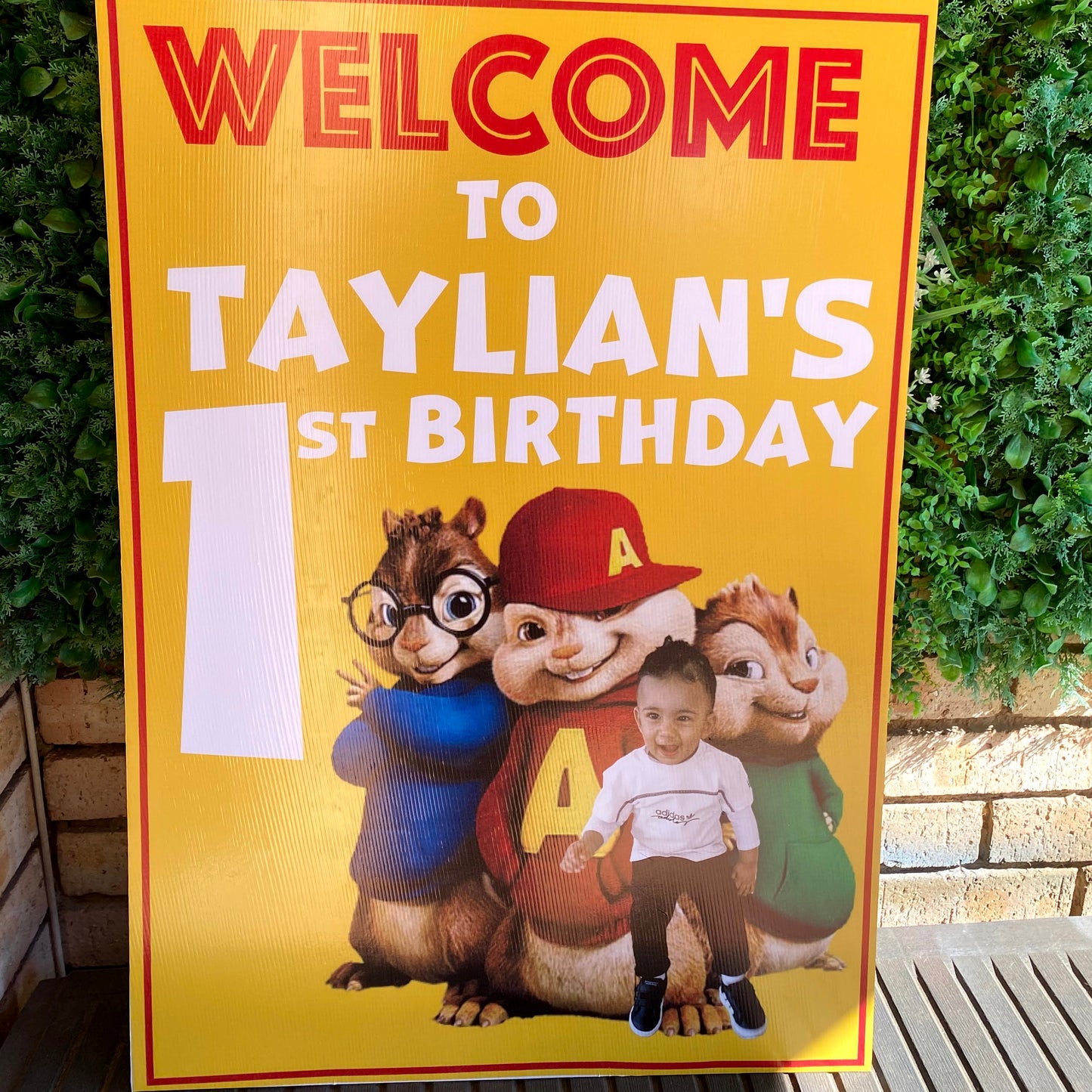 Birthday sign with cartoon characters on a yellow background, placed on green grass.
