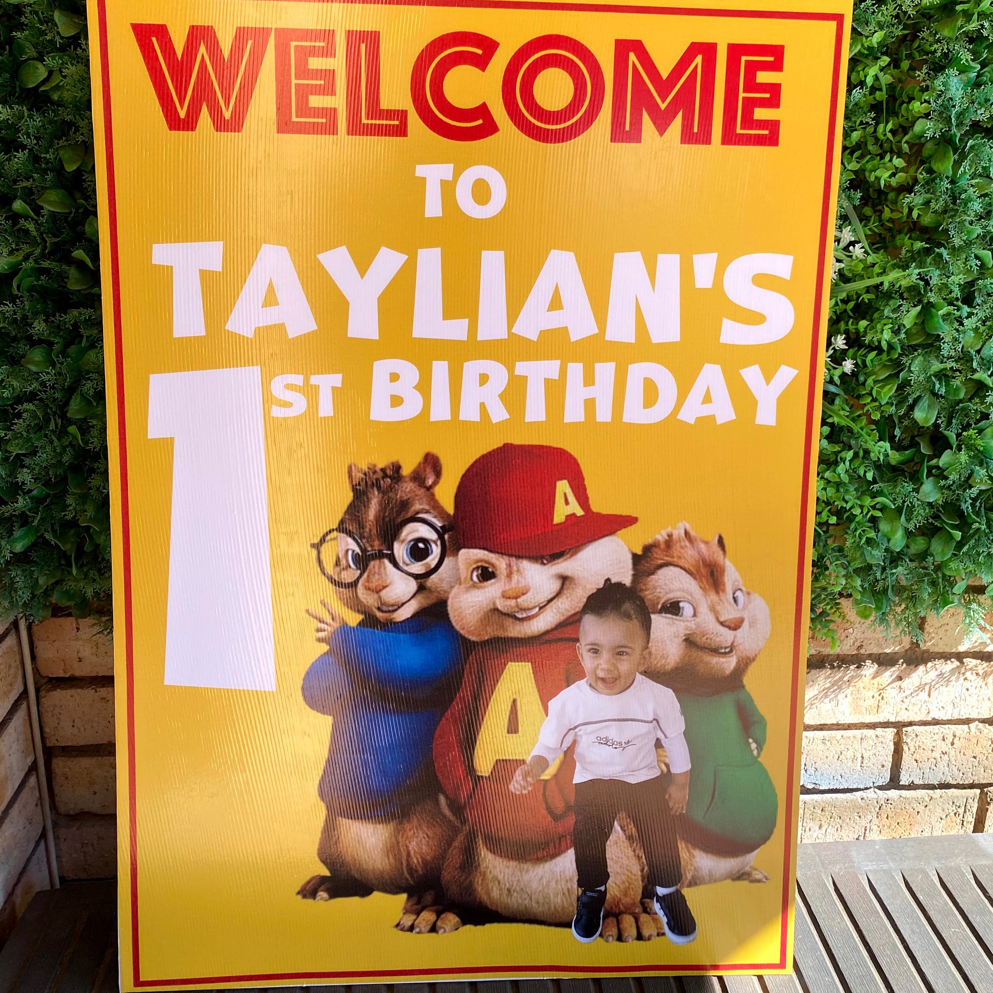 Birthday sign with cartoon characters on a yellow background, placed on green grass.