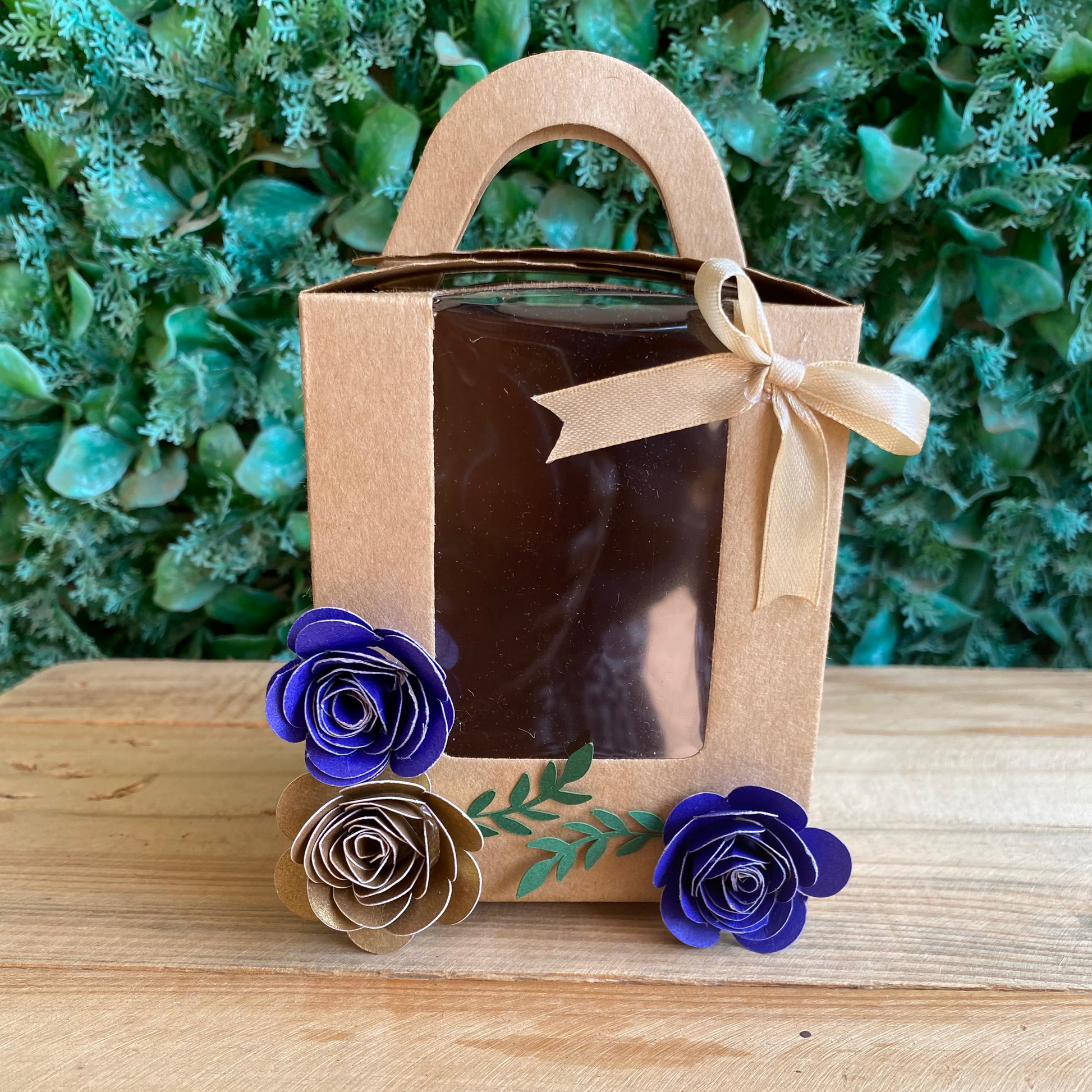 Gift box with decorative flowers on a wooden surface and green foliage background